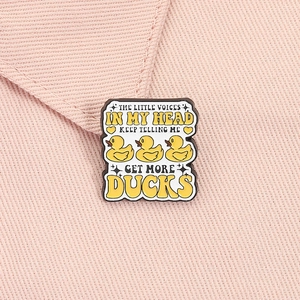 Detail of funny yellow duck enamel pin with creative text on pink fabric background