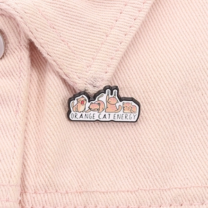 Macro shot of cute orange cat enamel pins with Orange Cat Energy text on pink denim jacket