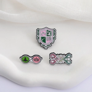 Macro shot of three pink and green enamel pins featuring shield and scissor designs