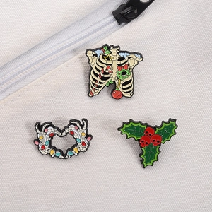 Close-up of enamel Halloween pins with skeleton ribs, heart hands and holly leaves