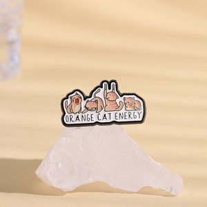Detail of enamel pin featuring four orange cats and Orange Cat Energy text on crystal