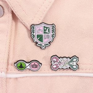 Detail of three-piece enamel pins set on pink denim showing crest, glasses and scissors