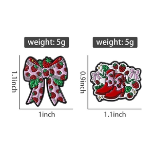 Detailed view of strawberry bow and boot enamel pins with precise measurements