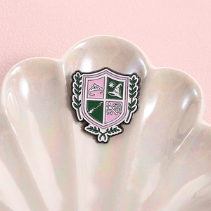 Cartoon shield enamel pin with magic crown and hat elements on pearlescent shell base