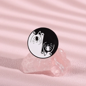 Yin Yang cat enamel pin displayed on pink crystal stone with warm shadow lighting