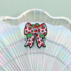 Pink bow brooch with strawberry pattern on an iridescent shell display tray