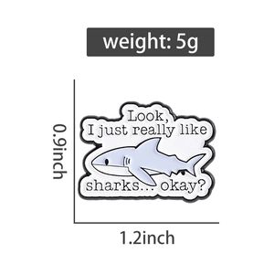Detail of shark enamel pin featuring blue shark graphics and funny quote text