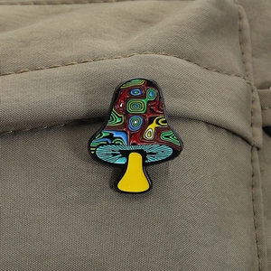 Detail of colorful mushroom enamel pin on a textured bag showing psychedelic swirl patterns