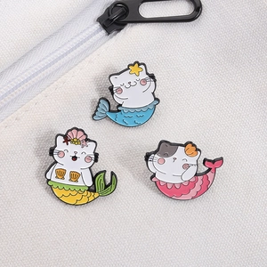 Vue détaillée de trois broches en émail de chat sirène coloré sur fond de toile blanche