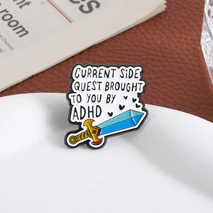 Detail of ADHD sword enamel pin with funny side quest text on a white ceramic plate