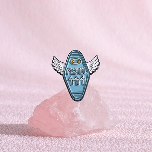 Detail of blue motel enamel pin with angel wings and number 444 on pink stone