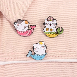 Detailed view of three colorful mermaid cat enamel pins on pink denim fabric background