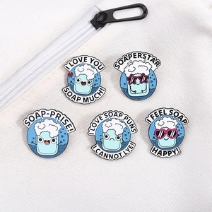 Flat lay of five creative cartoon soap enamel pins with cute puns on a white canvas background