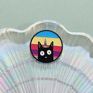Détail d'une broche ronde en émail chat licorne avec des rayures arc-en-ciel colorées