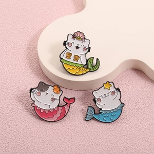 Trois pin's émaillés chat sirène en jaune, rose et bleu sur un fond texturé rose