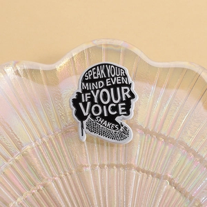 Detail of black enamel pin with motivational text SPEAK YOUR MIND EVEN IF YOUR VOICE SHAKES