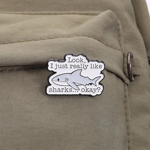 Détail d'un pin's en émail requin sur sac en toile avec citation drôle Look I really like sharks