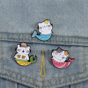 Trois broches chat sirène en émail fixées sur le tissu d'une veste en jean bleu