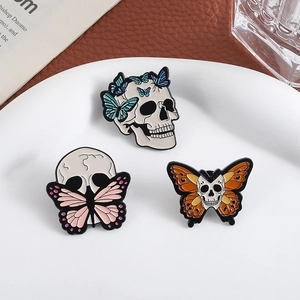 Three creative enamel pins featuring butterfly and skull motifs on a white plate