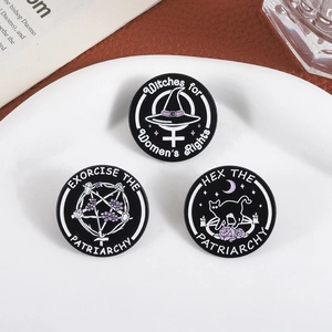 Detail of three black enamel badges with feminist witch themes on white ceramic plate