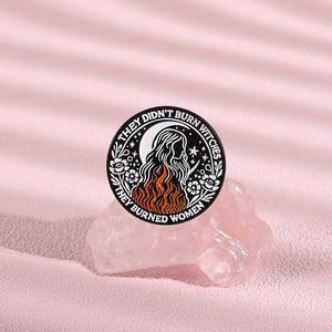 Detail of round enamel witch badge with floral patterns and feminist quote on pink crystal