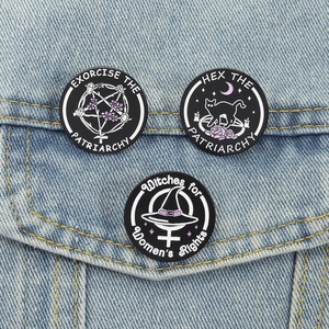 Close-up of three enamel mystical badges pinned on a denim jacket featuring witchy designs