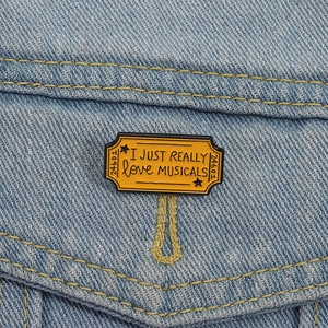 Broche en émail jaune forme timbre avec texte musical épinglée sur veste en jean