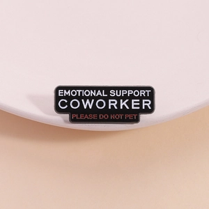 Black enamel brooch with Emotional Support Coworker text on a white curved tray