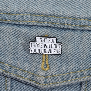 Enamel brooch with 'Fight For Those Without Your Privilege' text on denim jacket