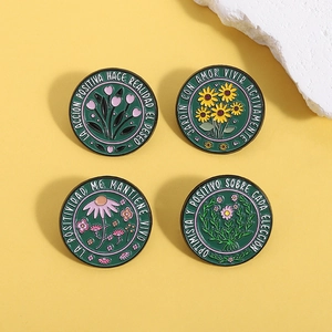 Detailed close-up of four green floral enamel pins with Spanish quotes on yellow background
