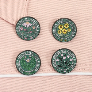 Detail of four floral enamel pins with Spanish quotes on pink textured fabric surface