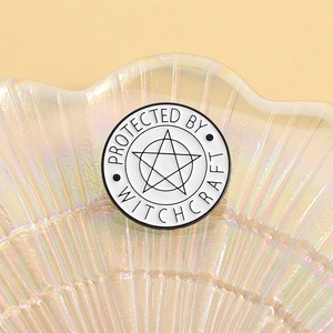 Close-up of circular enamel pin featuring Protected by Witchcraft text and star design