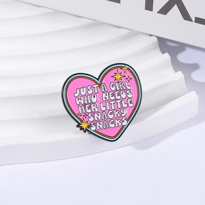 Dettaglio della spilla a cuore rosa smaltata con stelle e citazione 'snacky snacks'