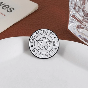 Detail of round black and white enamel pin with Protected by Witchcraft pentagram design