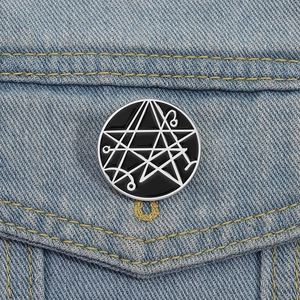 Enamel pin with geometric occult symbols on denim jacket, black and silver round brooch