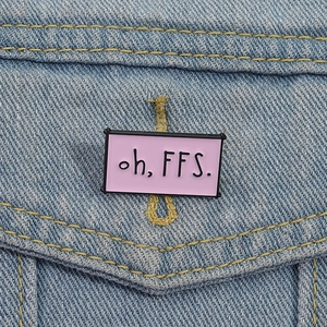 Pink rectangular enamel pin with oh, FFS. text pinned on blue denim jacket pocket