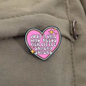 Dettaglio della spilla a cuore rosa smaltata con slogan su tessuto verde oliva