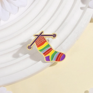 Rainbow knitted sock enamel pin with knitting needles on white podium display