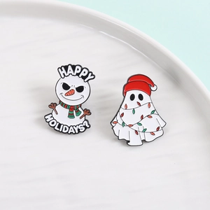 Christmas enamel pins featuring snowman with scarf and ghost with holiday lights on ceramic tray