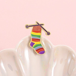 Rainbow striped sock enamel pin with knitting needles on a decorative shell