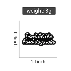 Detail of black enamel pin with white Don't let the hard days win quote and size specs