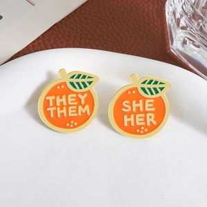 Lot de pins émaillés en forme d'orange avec pronoms She/Her et They/Them sur plateau