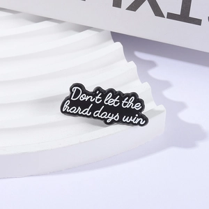 Minimalist black enamel inspirational quote brooch on white stone display stand