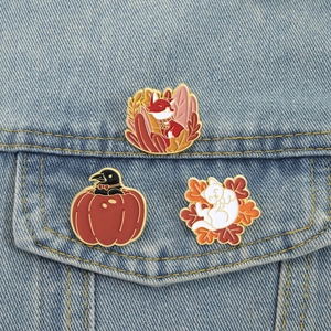 Detail of fox, crow, and cat enamel pins on denim jacket with autumn maple leaf design