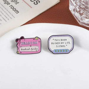 Bookworm enamel pins featuring Bookish Girlie and 5 Stars quote on white ceramic plate