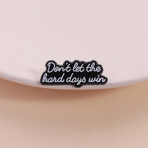 Minimalist enamel pin featuring white lettering Don't let the hard days win on black metal