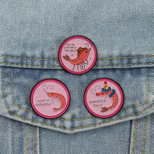 Detalle de tres pines de esmalte con juegos de palabras de gambas en una chaqueta