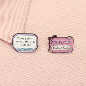 Détail de broches en émail rose pour les amoureux des livres sur tissu texturé