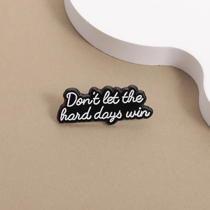 Close-up of black enamel brooch with white 'Don't let the hard days win' text