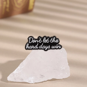 Detail of minimalist enamel pin with motivational text on white mineral stone